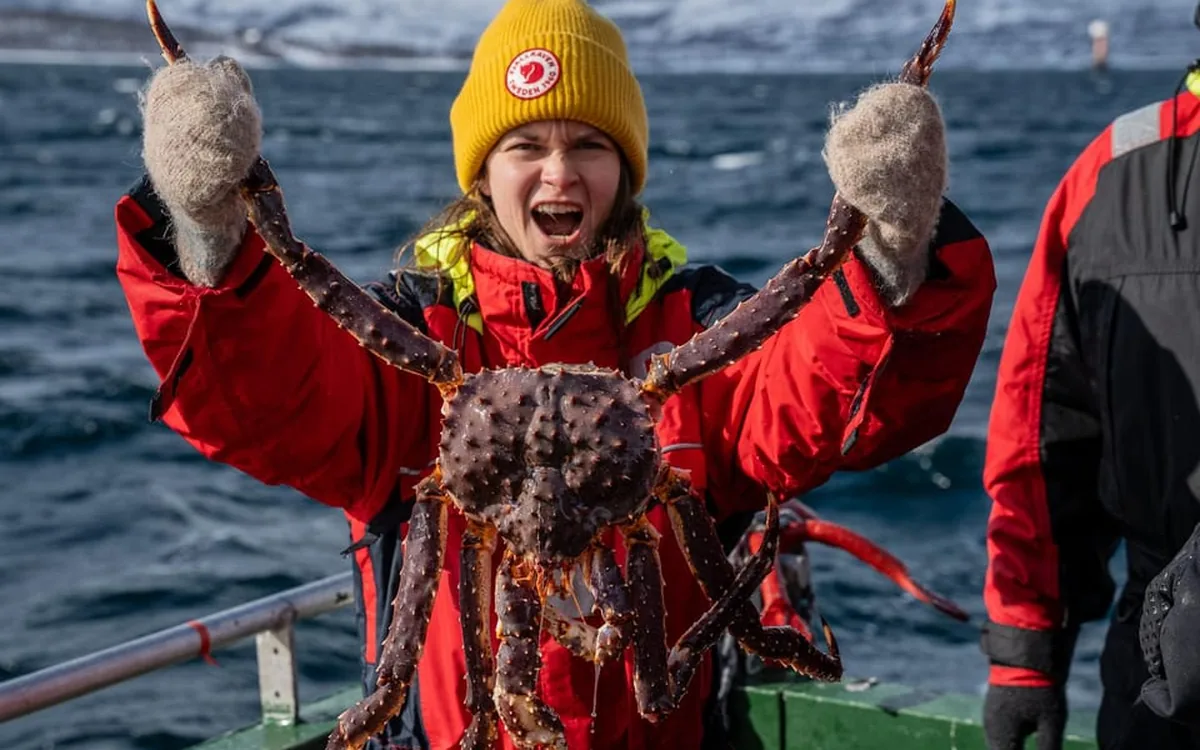 A guest in a yellow hat holding a king crab above her head