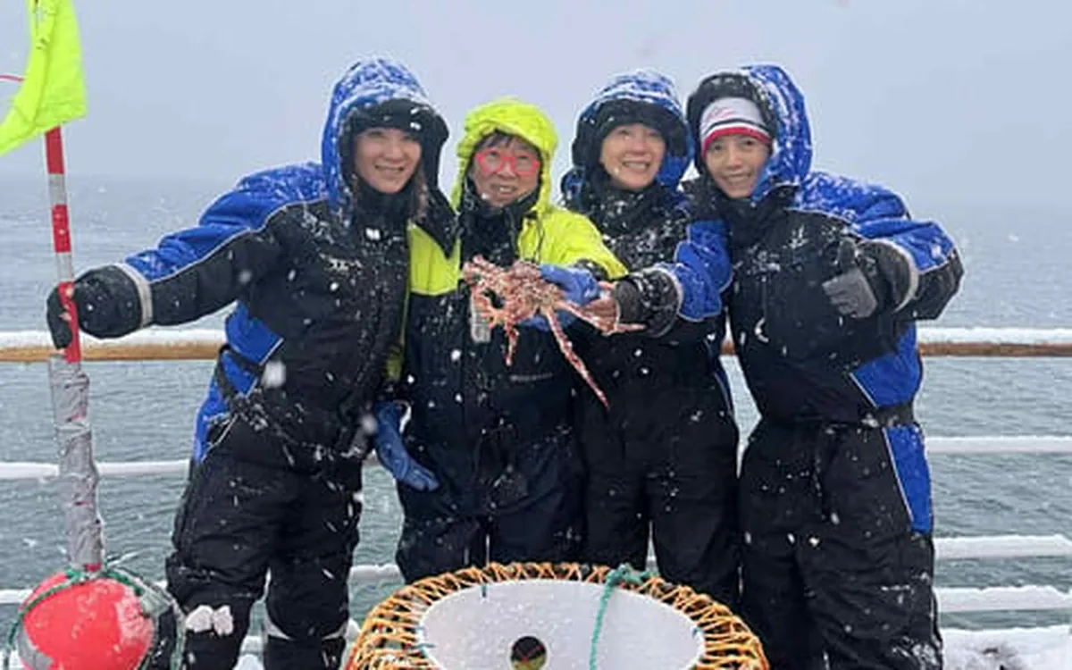 Four guests in insulated suits standing on deck with a crab pot