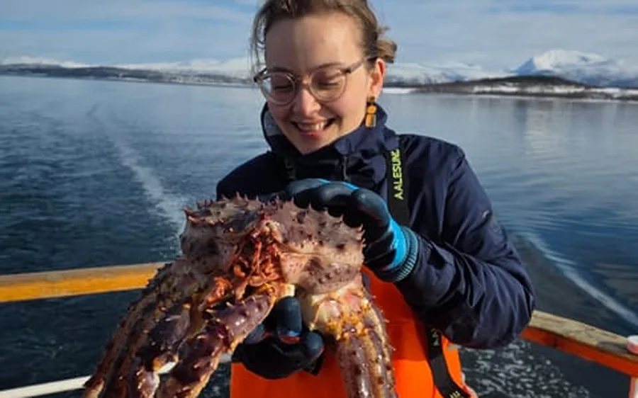 A guest holding a king crab with the fjord behind her