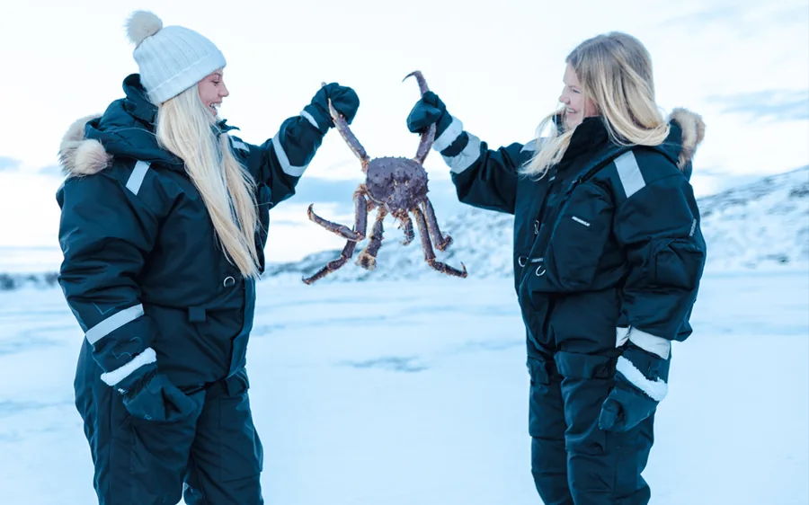 Two guests holding a king crab on the frozen fjord